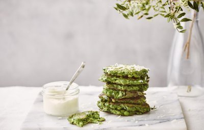 Enkele klaargemaakte fritters liggen gestapeld op een marmere snijplank. De fritters hebben een mooie groene kleur, er naast staat een glazen potje met de citroenmascarpone om te benuttigen als dip. 