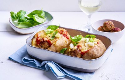 Op tafel staat een ovenschotel met hierin twee gepofte aardappelen, ze zijn gevuld met balletjes en tomatensaus. Ze kregen nog een kaaskorstje, lente-uiringen en basilicum. 