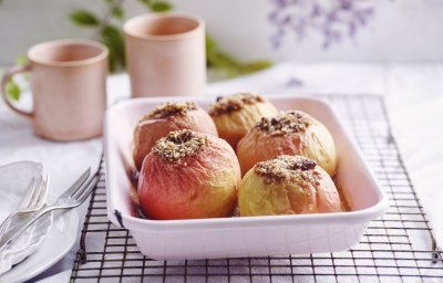 Gevulde appels in een licht roze ovenschaal. Achteraan staan twee roze kopjes, klaar om aan het ontbijt te beginnen.