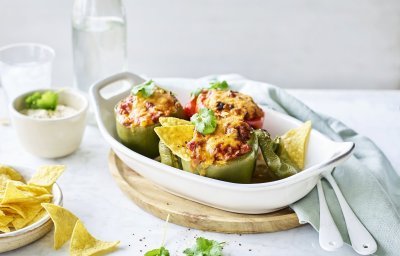 Een witte ovenschaal staat op tafel te blinken met opgevulde groene paprika's. Ze zijn gevuld met chili con carne en enkele nacho's. Dit is sowieso een gerechtje dat jong en oud niet koud laat. 