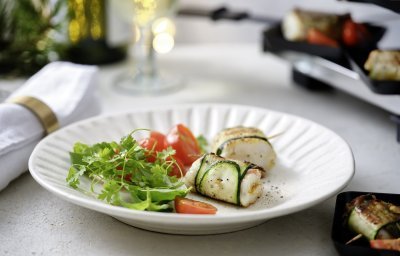 Twee pakjes liggen op een wit bord. Het pakje is gemaakt van een stukje vis verpakt in een sliertje courgette. We serveren dit feestelijk gerechtje met een frisgroene kruidensla en kertomaatjes.  