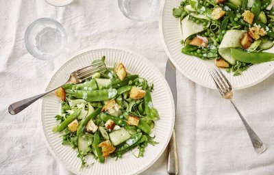 Twee bordjes staan op tafel met een wit linnen tafelkleed. De bordjes zijn fris van kleur door de verse groene groenten, de goudgebakken croutons zien er heerlijk uit.
