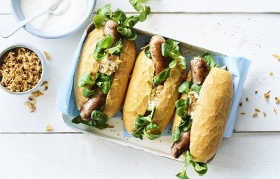 3 hotdogs liggen klaar om gegeten te worden. Ze zijn vergezeld met groene groentjes en een sausje. 