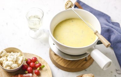 Op tafels staat een fondue-toestelletje met een wit steelpannentje op. Deze is gevuld met de kaasfondue, hierlangs liggen brood, radijsjes, tomaten enz. 