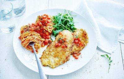 Op tafel staat een portie van de krokante kalfslapjes alla Milanese met tomatensalsa, pasta en rucola.
