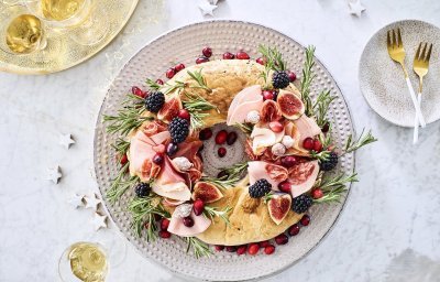 Een echte Kerstkrans om op te eten. De krans is gemaakt van een Turks brood die belegd werd met verschillende vleesjes, fruit en rozemarijn. Hij staat op de feesttafel en enkele zilveren sterren liggen er langs vergezeld met enkele aperitiefjes. 