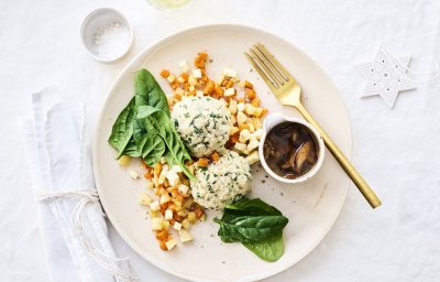 Knoedels, gemaakt van brooddeeg, liggen bovenop gestoofde blokjes peterseliewortel en zoete aardappel. Deze vegetarische ballen worden opgediend met een sausje van bospaddenstoelen. Het sausje staat mee op het bord in een potje. Goud bestek en kerststerren liggen langs het bord.