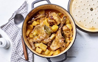Op tafel staat een gietijzeren pot gevuld met de ragout van konijn. Hij heeft een gouden kleur door de pastinaak, wortel en krieltjes. 