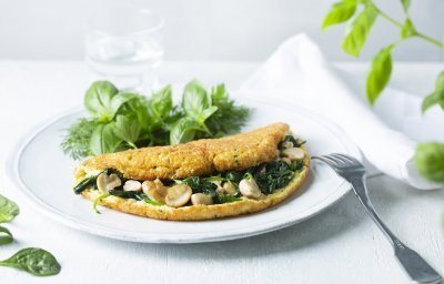 Een heerlijke dichtgevouwde omeletsoufflé gevuld met champignons, spinazie en kaas ligt op een wit bord. Het gerechtje werd afgewerkt met een slaatje van verse kruiden, denk maar aan basilicum en dille.  