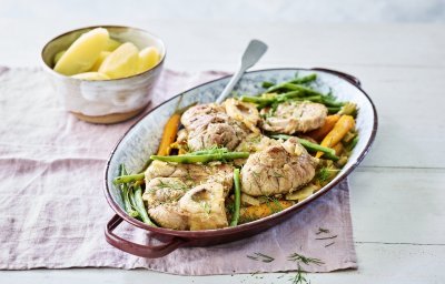 De kalfsschenkels liggen in een ovenschotel met groene boontjes en oranje wortels erbij. Dit zorgt voor een mooie variant op de klassieke ossobuco.