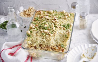 De ovenschotel met pulled chicken en knolselderpuree staat op tafel, hij is afgewerkt met hazelnoten en peterselie wat een mooie kleur geeft. Er ligt een lepel langs op een klein bordje om meteen uit te scheppen en met het hele gezin aan tafel te gaan.