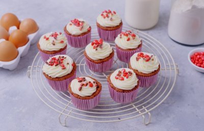 Cupcakes staan op een witte taartrooster om af te koelen. Ze zijn afgewerkt met mooie toefjes frosting en gecrushte rode smarties.  