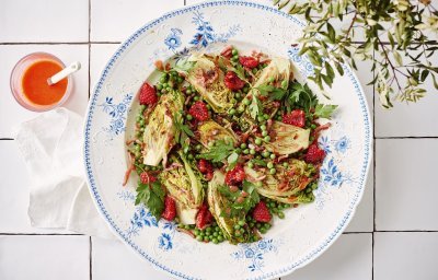 Een wit retro bordje staat op het aanrecht. Het is gevuld met een salade, gebakken spekjes en little gem. De frambozendressing is helder en roze, deze staat naast het bord in een glazen potje. 