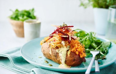 Gepofte zoete aardappel met wortelen, radijsjes, rode biet en appel gepresenteerd op een blauw bord met een rucola slaatje als bijgerecht.