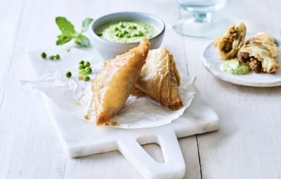 Klaargemaaakte samosa met lamsvlees liggen gepresenteerd op een marmer plankje. Ze worden opgediend met een frisgroene dip van munt en erwtjes.