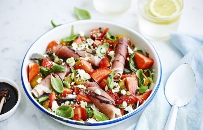 Rijkgevulde salade met aardbeien, geitenkaas en gandaham. Afgewerkt met balsamico. Er zijn twee frisse waters boven de kom met elk een citroentschijfje in. 