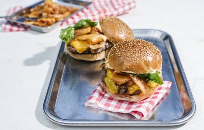 Twee hamburgers liggen op een inoxe plateau. De ene burger moet zijn hoedje nog krijgen.