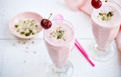 Twee rooskleurige smoothies op een witte houten tafel. De smoothie is afgewerkt met een kers en enkele pitjes en zaadjes. Een snel en makkelijk drankje met feestallures! 