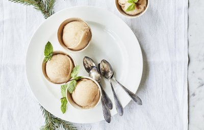 Drie sorbets staan op een wit rond bord, afgewerkt met een muntblaadje. De koffielepeltjes liggen ook op het witte bord, de tafel is aangekleed met takjes kerstboom.