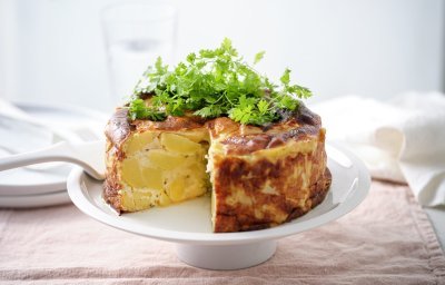 Op een witte taartschaal staat een heerlijk klaargemaakte aardappeltaart met stukjes schorseneren en wat geitenkaas. We werkten hem af met een handje verse kervel.