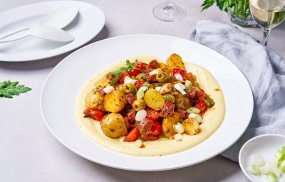 Een grote witte serveerschaal is gevuld met de aardappelsalade. Er werd eerst aioli opengesmeerd waarop de aardappelen, paparika, tomaatjes, olijven en chorizo op liggen. Een heerlijk bijgerecht met vele zuiderse smaken. 