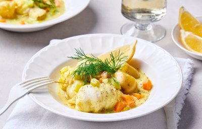 Een wit diep bord staat op de tafel, hij is gevuld met een geelkleurig stoofpotje van vis door de curry. Het visstoofpotje is afgewerkt met dille en een partje citroen.