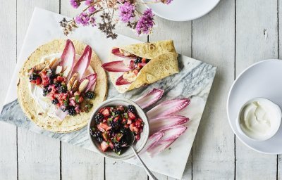 Taco’s met kip, roodlof en een salsa van braambessen en aardbei ligt klaar om op te eten. Er ligt al een tweede taco in de maak, op een marmere snijplank. De kleuren van roos tot donker rood van het fruit en loof geven een mooi contrast in de foto.