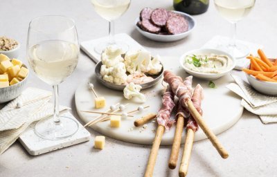 Een mooie marmere serveerplank in rond vorm staat op tafel. Hij is gevuld met allerlei tappas, zoals bloemkoolroosjes met cocktailsaus, wortel, kaasblokjes, salami met mosterd en homemade hummus.