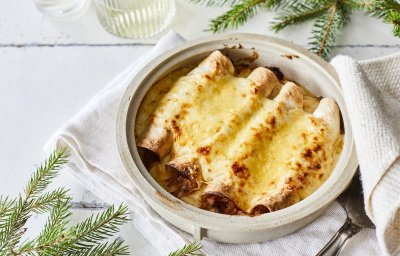 Opgerolde wraps gevuld met traagggegaard vlees liggen netjes naast elkaar in een ovenschotel. Hierover is kaassaus geserverveerd en even gegrild. Perfecte snack als bijgerechtje op je feesttafel, heerlijk voor groot en klein. 