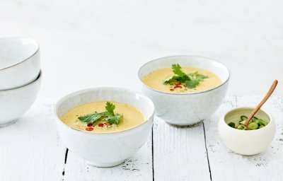 Thaise tomatensoep in twee kommetjes uitgeschonken. Topping van chilipeper en koriander ligt mooi in het midden van de soep. Alles staat op een witte houte tafel.