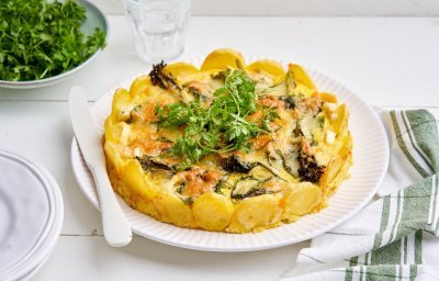 De tortilla ligt op een groot wit bord, er zijn aardappelschijfjes gebruikt als bodem maar ook als rand. Dit geeft een mooi beeld om naar te kijken. De taart is gevuld met prei, broccolini en spinazie, boordevol groenten. We serveren hem nog met wat kervel om het af te werken. 