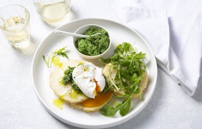 Traaggegaarde knolselderschijven liggen op een groot wit bord vergezeld met een gepocheerd ei en pesto van boerenkool in een wit potje. Er is ook nog wat rucola toegevoegd voor de extra groene toets.   