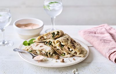 De turkse pannenkoek gevuld met gehakt, spinazie en feta ligt op een wit bord. Er ligt een roze servette langs en het chili-dipsausje staat bovenaan. 