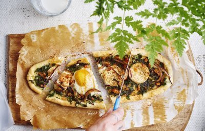 Een hartige Turkse groententaart met spinazie, geitenkaas en ei ligt op een houten snijdplank. Ze wordt aangesneden met een mes. 