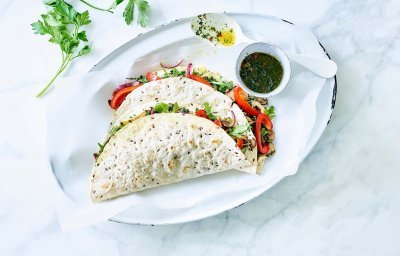 Vegetarische quesadilla gevuld met geroosterde knolselder, champignons, paprika en Brugge Oud. 2 stuks liggen gepresenteerd op een ovaal wit bord, samen met de vinaigrette in een potje apart. Takje verse koriander ligt er langs voor extra groen en sfeer aan het beeld mee te geven.