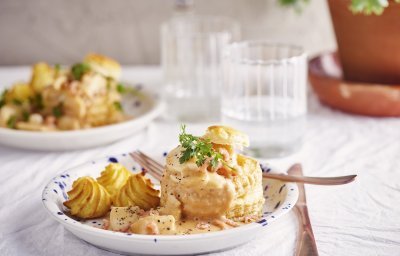 Twee borden staan klaar om van te smullen. Vol-au-vent van vis in een bladerdeegpasteitje met pommes duchesse. Er staat een glaasje water naast het bord.