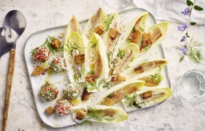Op een rechthoekige dienschotel liggen meerdere blaadjes van witloof gevuld met een stukje sprot, ringen van sjalot en croutons. In het hoekje van de schotel liggen de roomkaasballetjes, deze balletjes zijn gerold in roze peperkorrels en verse dille waardoor ze als het ware een jasje van kruiden kregen.