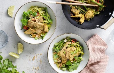 Twee bordjes zijn staan op tafel naast de wokpan, het gerechtje heeft een mooie groene kleur door de grote hoeveelheid groenten. 