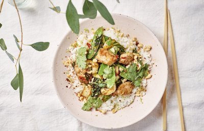 Een portie food is uitgeschept in een licht roze bord. Het is een portie rijst met daar bovenop de wok van konijn met paksoi en peultjes. Om af te werken zijn er wat pindanootjes toegevoegd en koriander.