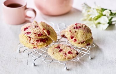 Op een kleine taartrooster liggen enkele koekjes te drogen. De koekjes hebben rode vlekjes van de framboosjes. Er staat een theepot langs met al een uitgeschonken thee in bijpassende roze tas. 