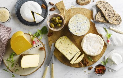 Kaasschotel op marmeren keukenblad. Verschillende Belgische kazen liggen op houten planken met brood, noten, radijzen en chutney erbij. 