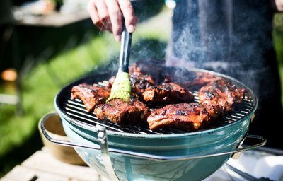 Ribbetjes op een barbecue in de tuin. De kok borstel nog wat marinade op het vlees.