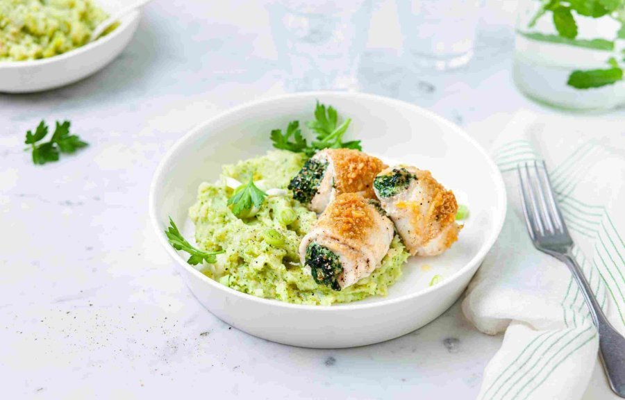 Gevulde tongrolletjes met spinazie en ricotta liggen op een groene puree van broccoli en aardappel. Ze liggen in een diep bord waarbij een karaf- en waterglas langs staat.