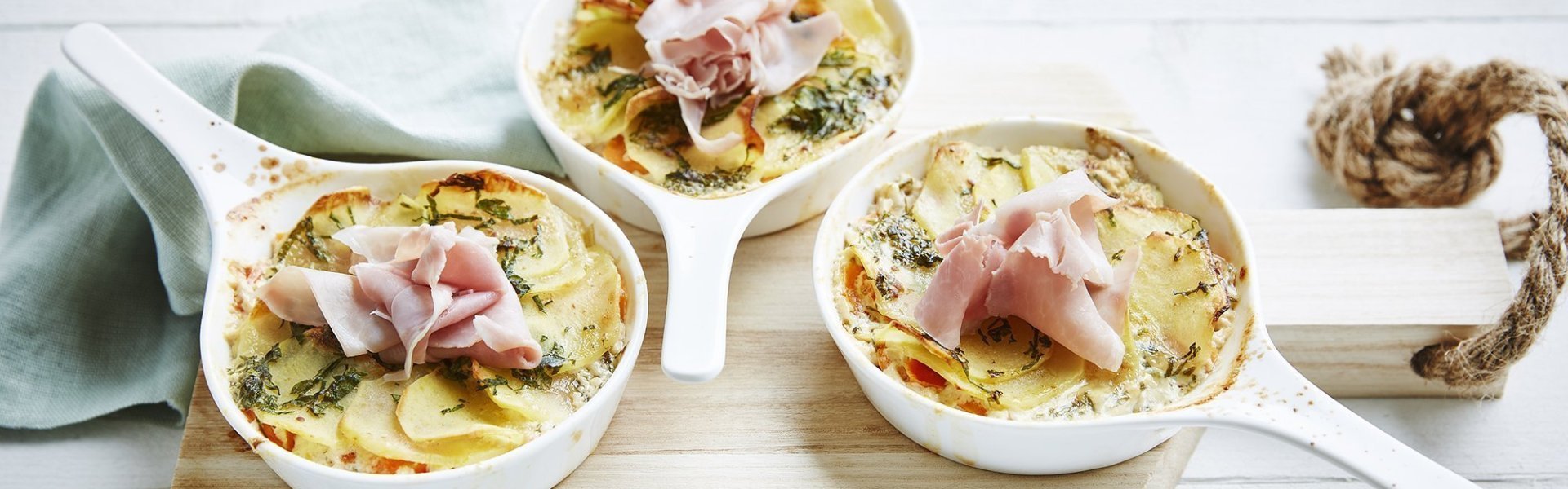 Aardappelgratin met wortel en witloof Kleine kommetjes met aardappelgratin, wortel en witloof op houten plankje. Geserveerd met een schelletje gekookte ham en verse tijm.