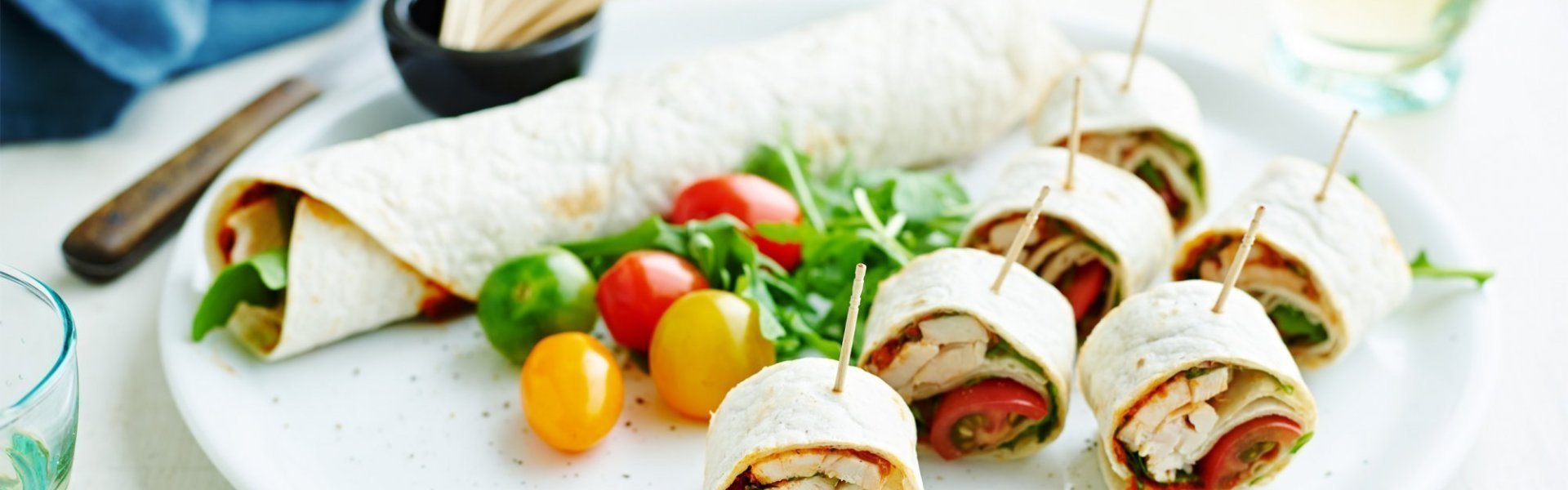 Op een bord ligt een rol wrap met groenten, wat kerstomaten en zes stukken wrap met een prikker in. Op een bord ligt een rol wrap met groenten, wat kerstomaten en zes stukken wrap met een prikker in.