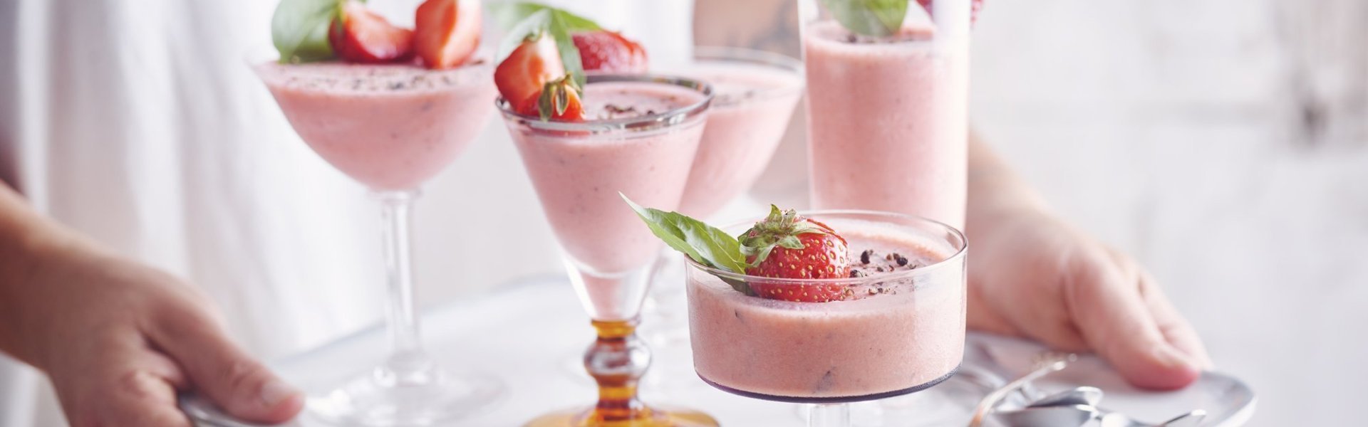 Bavarois van aardbei met basilicum en zwarte peper Roze bavarois geserveerd in verschillende glaasjes op een dienplateau. Een vrouw met witte t-shirt draagt deze roze dessertjes, klaar om naar de gasten te brengen.