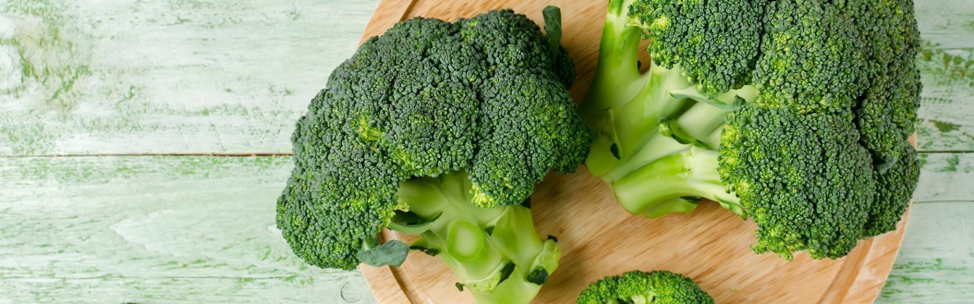 Twee groene broccoli's liggen op houten snijplank, klaar om roosjes uit te snijden en klaar te maken.