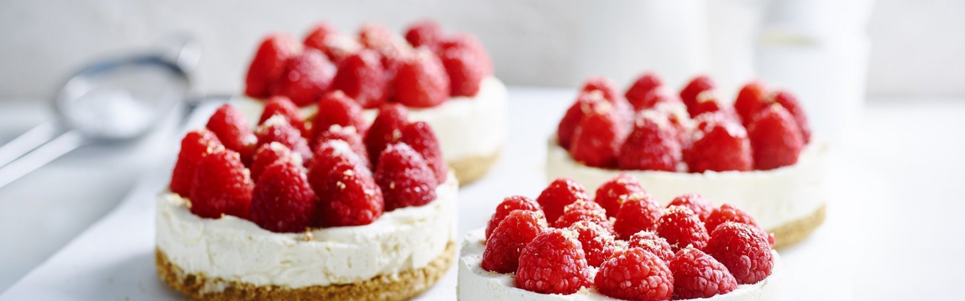 No bake-cheesecake met witte chocolade en frambozen Wij maakten 4 kleine cheesecakes en staan op een wit boterpapiertje. Ze zijn afgewerkt met verse frambozen die een mooi contast geven met het witte van de kaas.