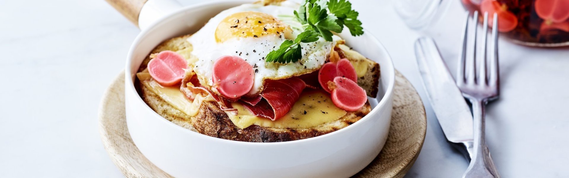 Croute au fromage met Averbode kaas, spiegelei en gepekelde radijs Croute au fromage met Averbode kaas in een witte pan, spiegeleitje er bovenop gepresenteerd met een takje verse peterselie. Op de achtergrond staan gepekelde radijzen in glazen pot.
