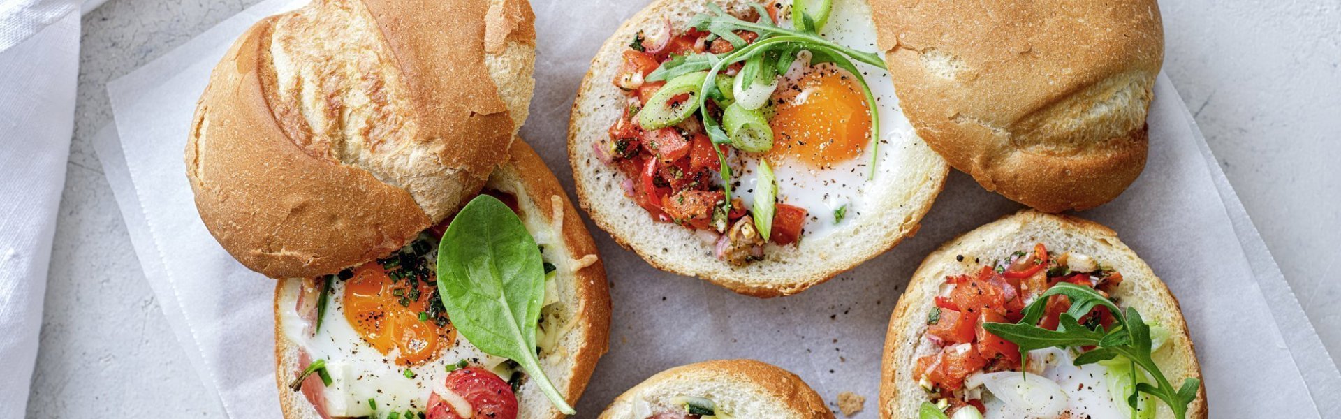 Eieren uit de oven met ham of tomatensalsa Gevulde broodjes met een eitje erin, staan op tafel te blinken! We maakte een versie met gekookte ham, courgette en tomaatjes. En onze tweede is er eentje met pittige tomatensalsa en rucola, heerlijk!